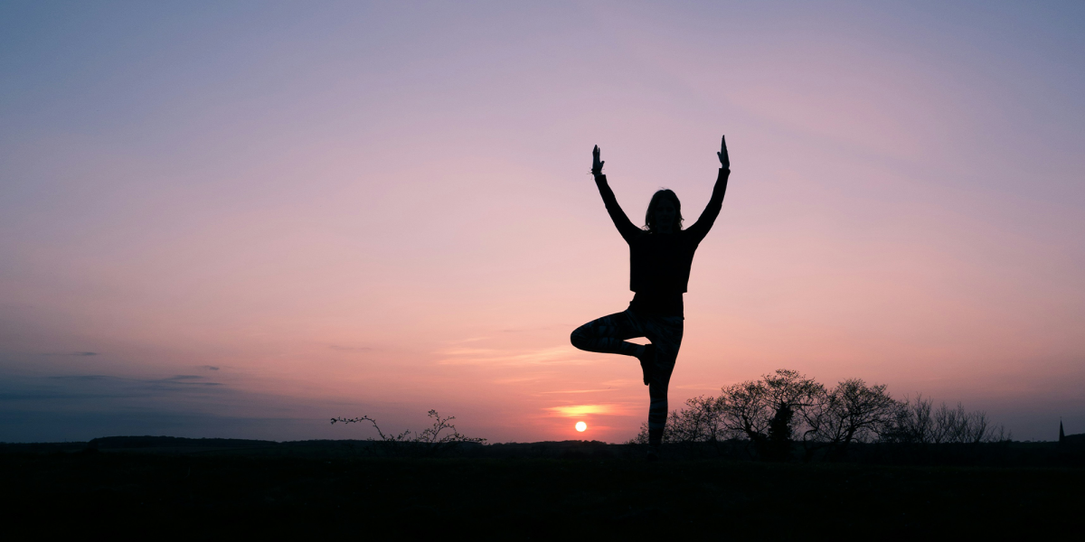 Silhouette of someone practising yoga against the sunset.