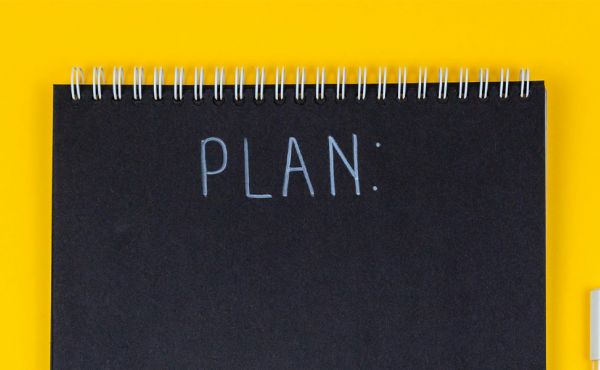Black notebook with the word 'Plan' behind the yellow desk.