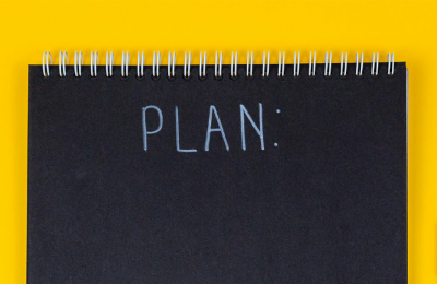 Black notebook with the word 'Plan' behind the yellow desk.