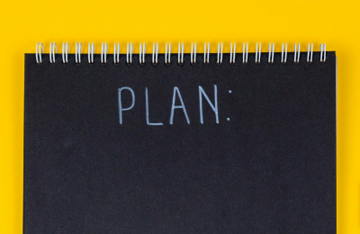 Black notebook with the word 'Plan' behind the yellow desk.