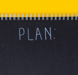 Black notebook with the word 'Plan' behind the yellow desk.